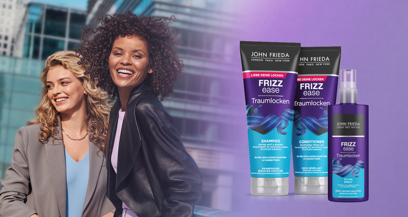 Zwei lächelnde Frauen mit Locken neben der John Frieda Frizz Ease Traumlocken Produktlinie, bestehend aus Shampoo, Conditioner und Spray.